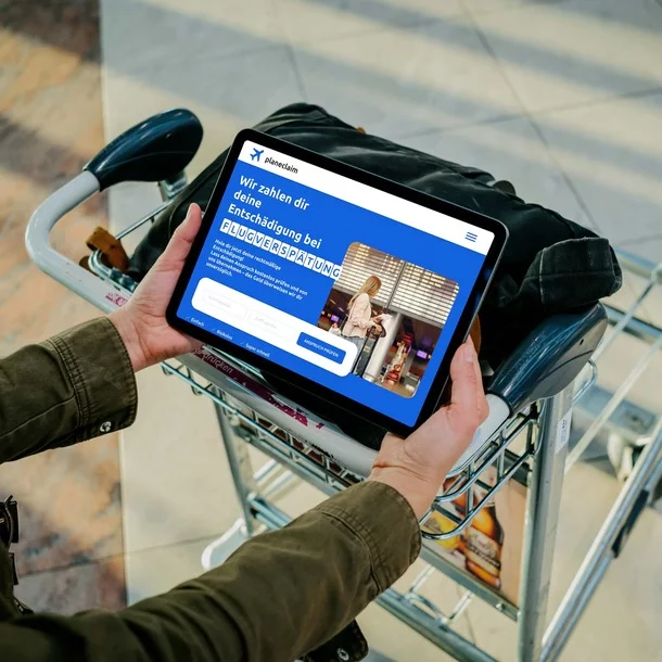 Person am Flughafen hält ein Tablet und holt sich seine Entschädigung für einen verspäteten Flug