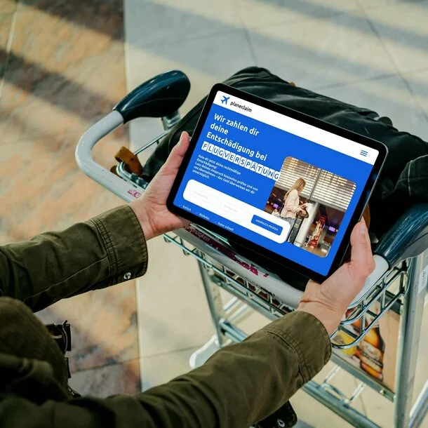 Person am Flughafen hält ein Tablet und holt sich seine Entschädigung für einen verspäteten Flug