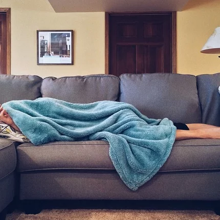 Das hilft gegen einen Jetlag Person mit starkem Jetlag liegt auf dem Sofa und versucht endlich schlafen zu können
