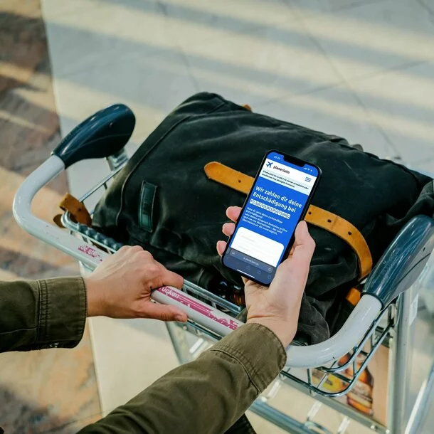 Person am Flughafen hält ein Handy und holt sich seine Entschädigung für einen verspäteten Flug