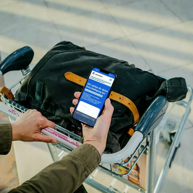 Person am Flughafen hält ein Handy und holt sich seine Entschädigung für einen verspäteten Flug